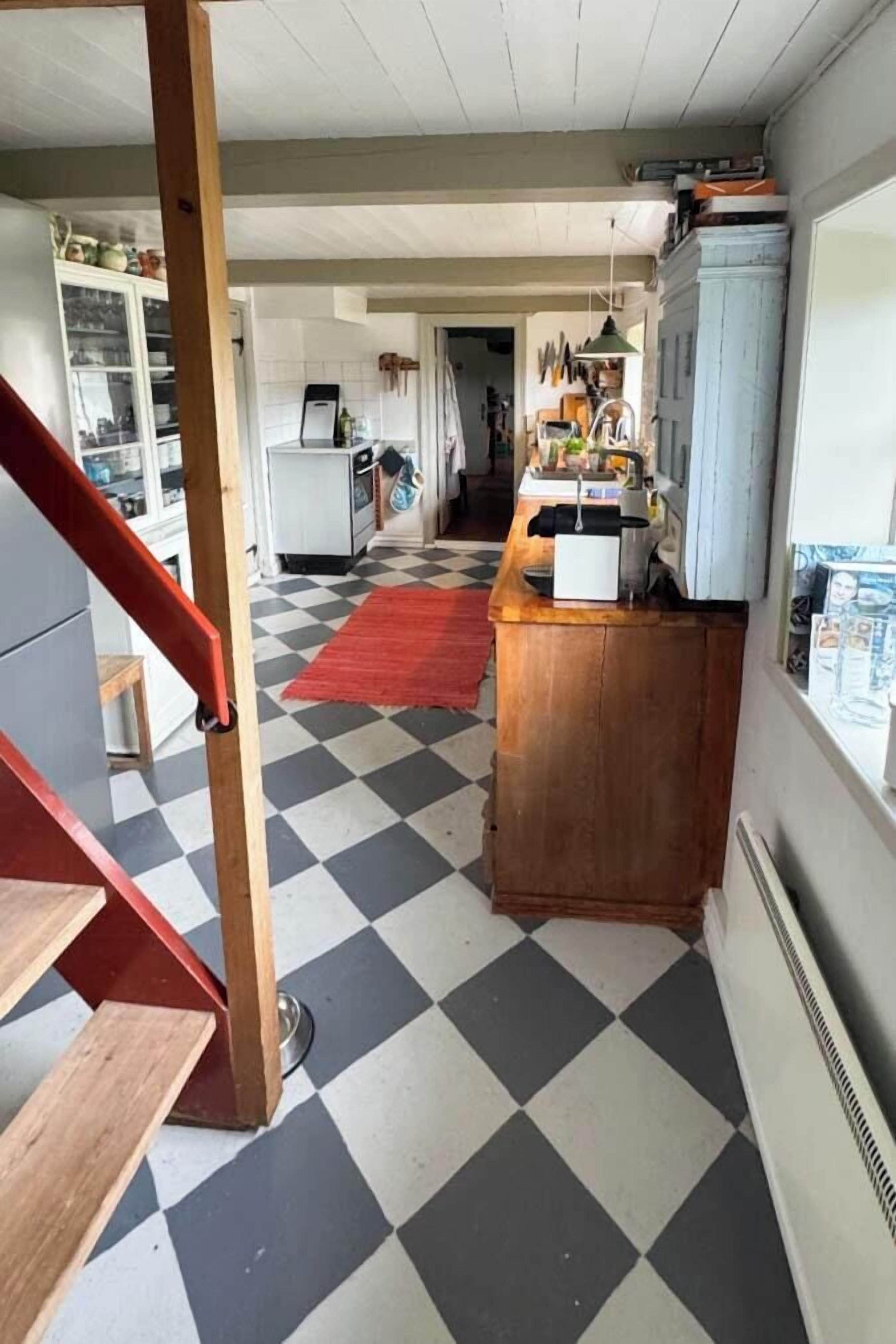 Une cuisine avec un carrelage à motifs, un comptoir en bois et un tapis rouge.