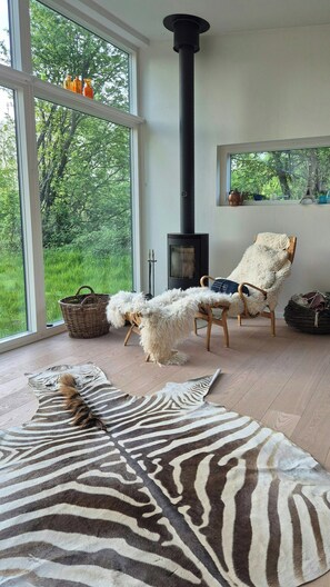 Ein Zimmer mit großem Fenster, Kamin, einem zebra-gemusterten Teppich und einem Sessel mit flauschigem weißen Bezug.