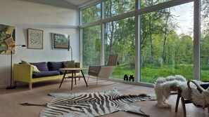 Ein modernes Wohnzimmer mit großem Fenster, einer Couch, einem Sessel und einem Hund.