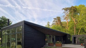 Ein modernes Gebäude mit großen Fenstern, einer flachen Dachkonstruktion und einer kleinen Außenbereich-Sitzgruppe.