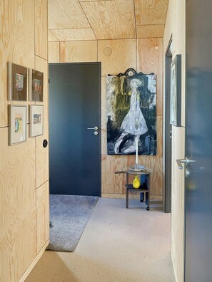 A hallway with wooden paneling, a dark door, and a painting on the wall. - Wooden home among apple trees with ocean view (Kivik)