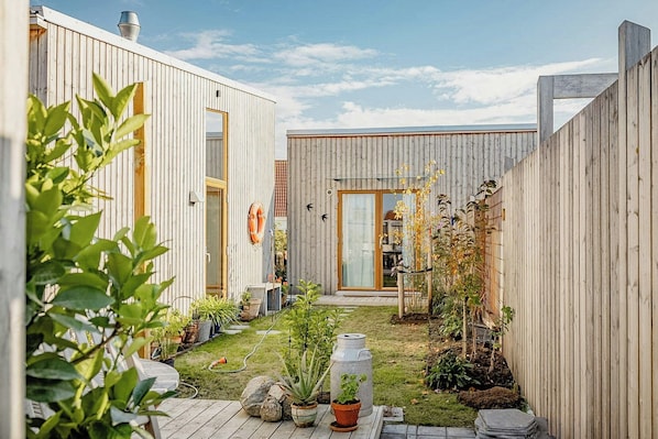 A modern outdoor space with wooden fencing, potted plants, and a small garden area. - Wooden home among apple trees with ocean view (Kivik)