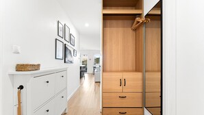 Un pasillo estrecho con un armario blanco a la izquierda, un guardarropa de madera a la derecha y cuadros en la pared.