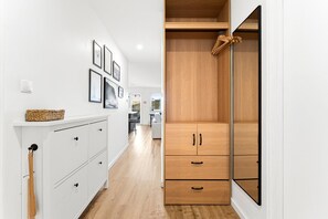 Ein schmaler Gang mit einem weißen Schrank links, einem Holzschrank rechts und gerahmten Bildern an der Wand.