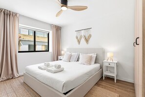 Ein modernes Hotelzimmer mit einem großen Bett, einem Nachttisch mit Lampe, einem Deckenventilator und Blick auf die Stadt durch das Fenster.