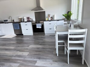 Uma cozinha moderna com forno embutido, armários brancos e uma área de jantar com mesa e cadeiras.