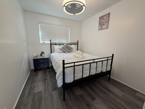 Quarto com cama, mesa de cabeceira, janela e uma obra de arte na parede.