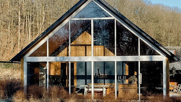 Une maison moderne dotée d’une grande façade en verre, entourée d’un paysage enneigé.