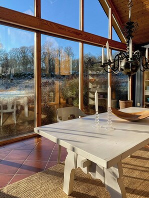 Ein Essbereich mit Tisch, Stühlen, einer Kandelaber und großen Fenstern mit Blick ins Freie.