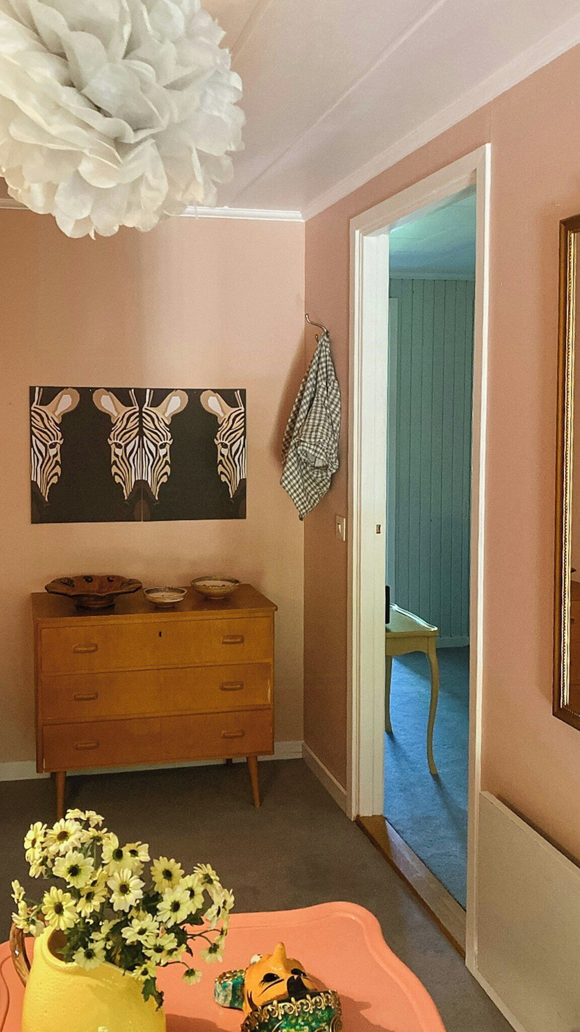 Una habitació amb un armari de fusta, un mirall, una obra d'art a la paret i una porta que dóna a un altre espai.