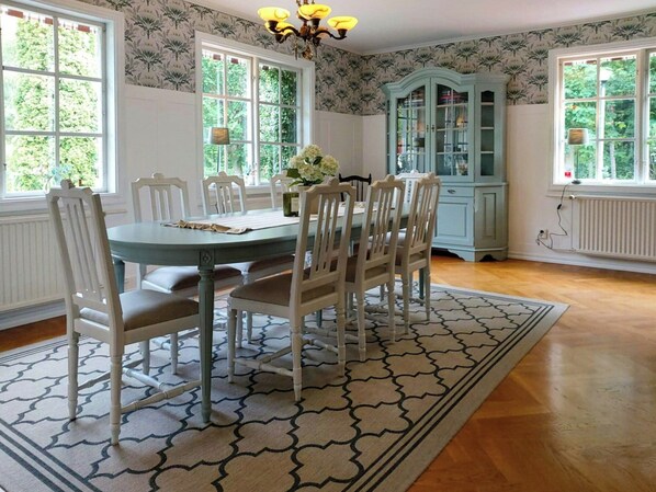 A dining room with a round table, white chairs, a patterned rug, and a blue cabinet.