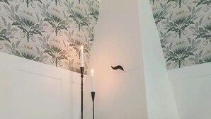 Une cheminée en briques avec un manteau de cheminée blanc, une bougie et un motif décoratif sur le mur.
