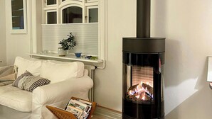 En stue med sofa, kæledyrs seng, en reviststativ, pejs og et vindue med persienner.