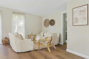 Ein Wohnzimmer mit einer Couch, einem Korbsessel, einem kleinen Tisch und einem gerahmten Bild an der Wand.