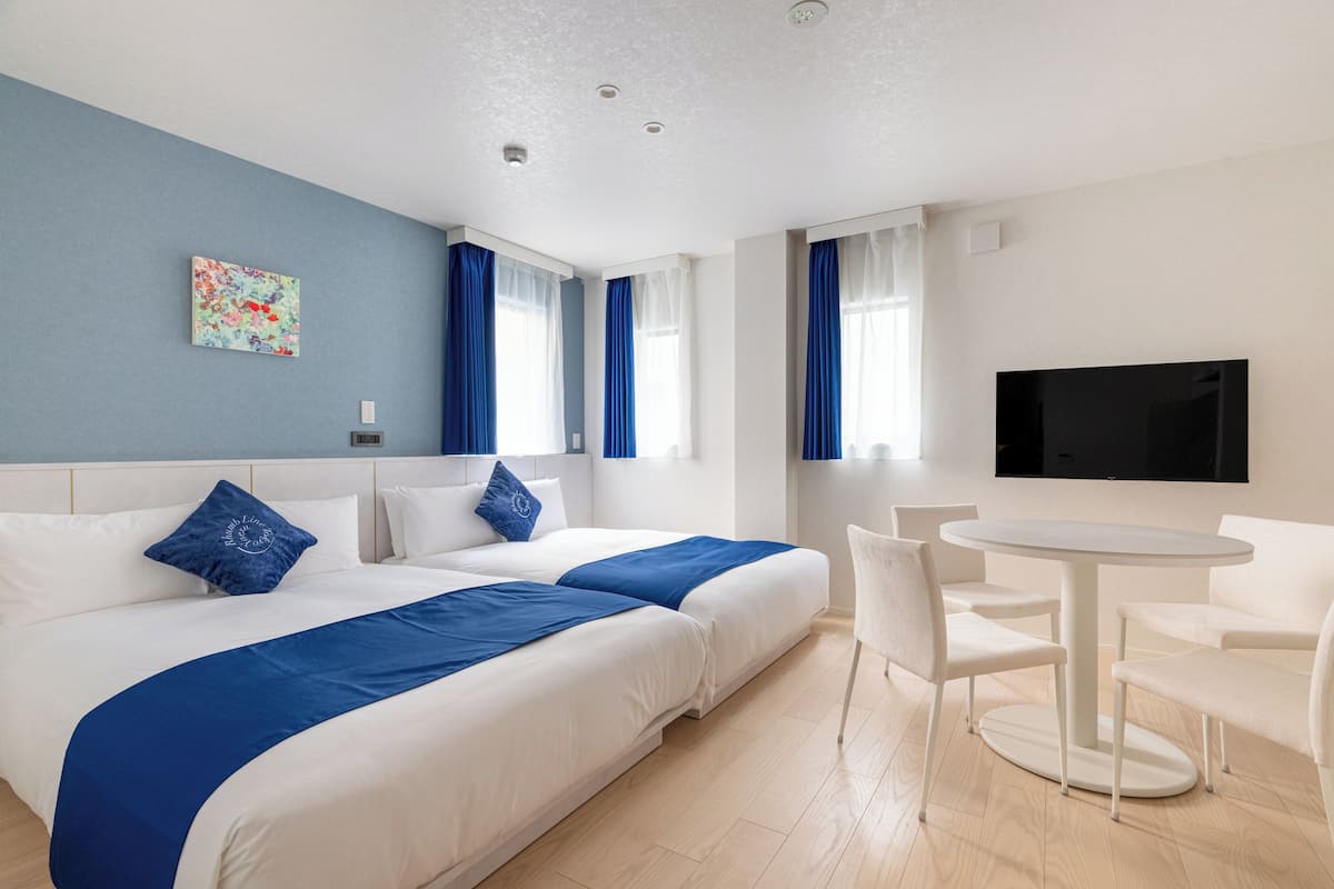 A hotel room with two beds, a TV, a dining table, and a window with curtains.