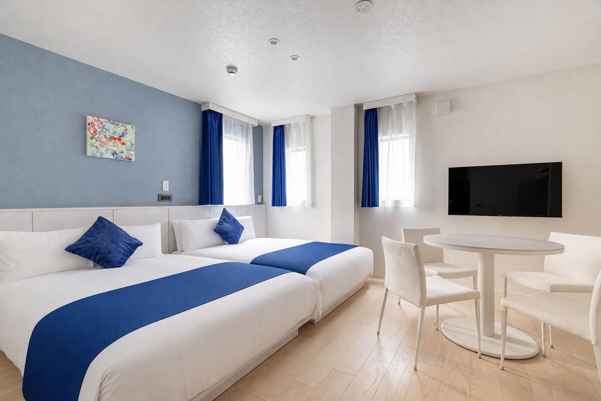A hotel room with two beds, a TV, a round table, and a chair.