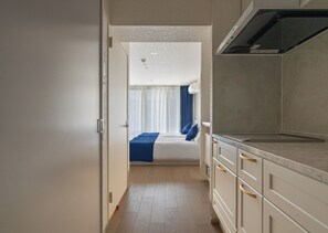 Un pasillo estrecho que conduce a un dormitorio con cama, una ventana con cortinas y una kitchenette con armarios y encimera.