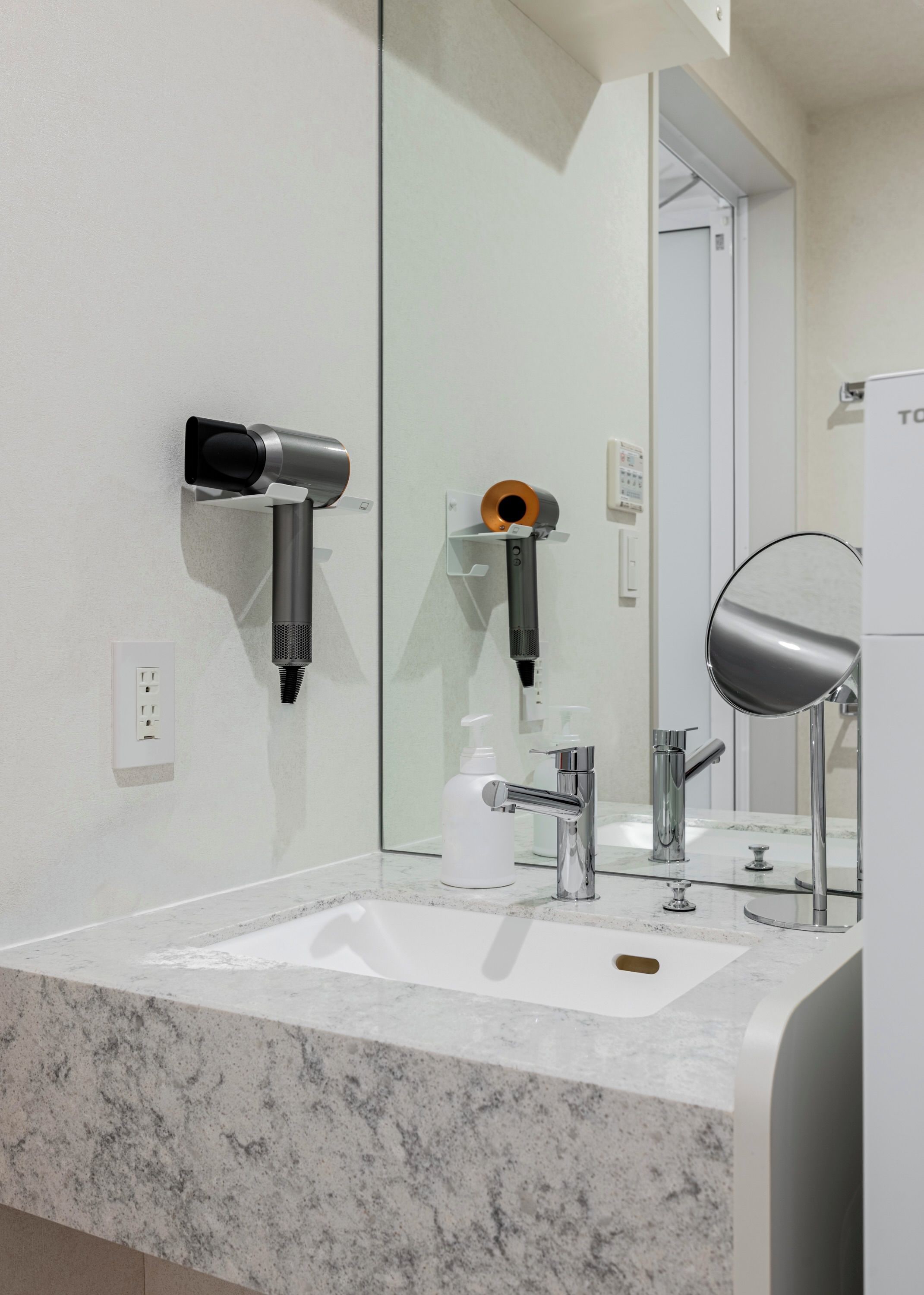 Un baño con un lavamanos blanco, un espejo, un secador de pelo y un dispensador de toallas.