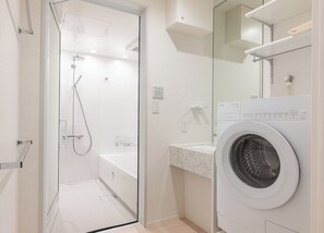 Un baño moderno con ducha envuelta en cristal, bañera blanca, lavadora integrada y encimera de mármol.