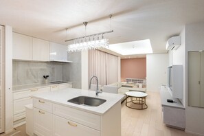 Una cocina moderna con armarios blancos, una isla central con pileta, una araña y un comedor con mesa redonda.