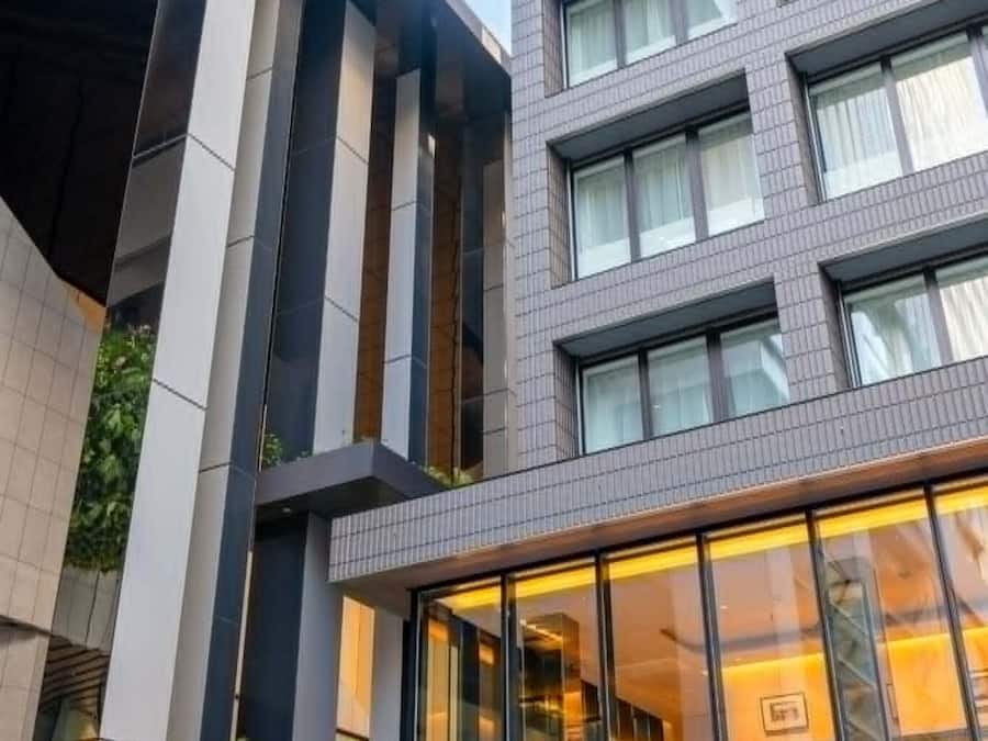 A modern building with a glass facade, vertical lines on the facade, and a balcony with a railing.