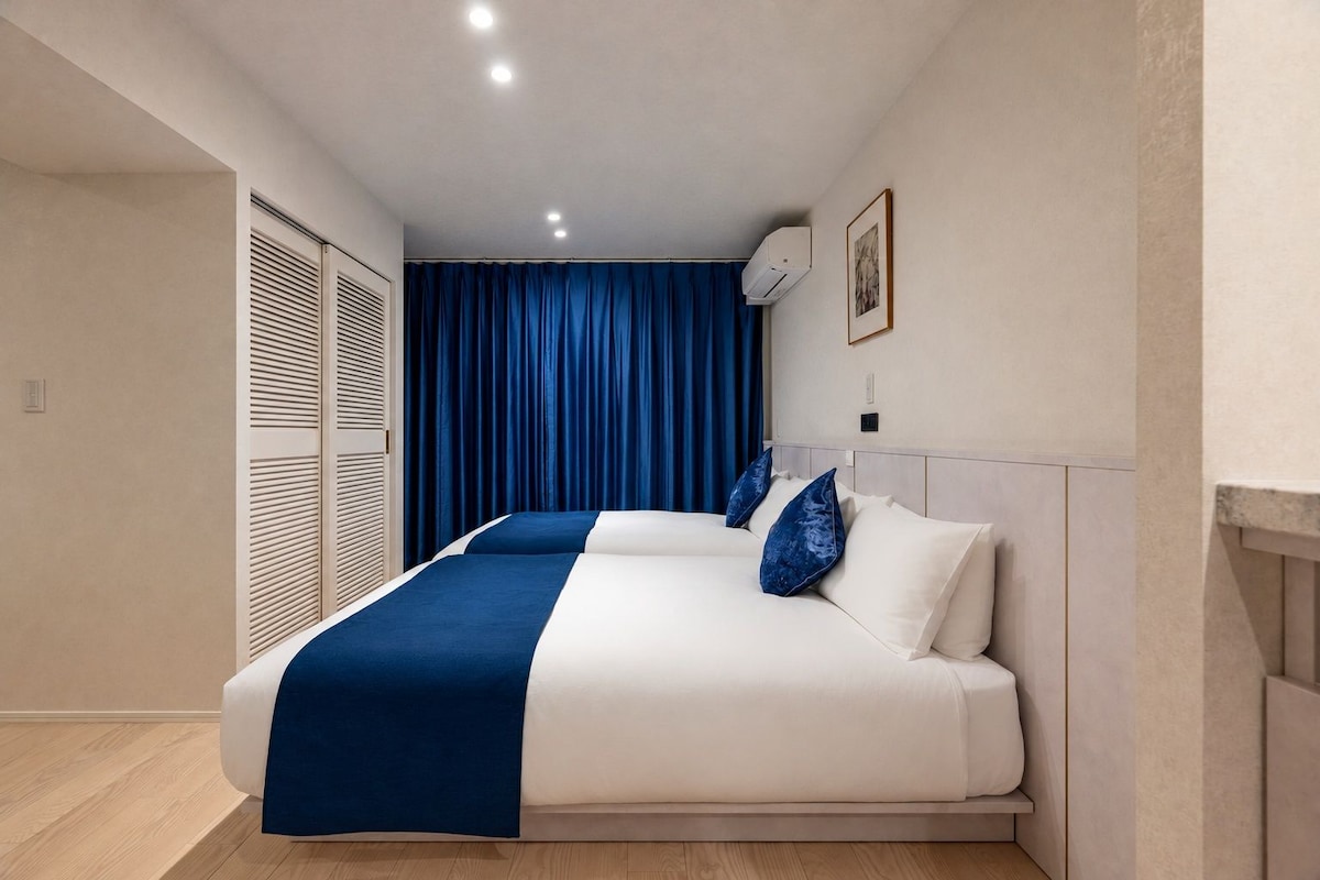 A hotel room with a bed, a window with curtains, an air conditioning unit, and a framed picture on the wall.
