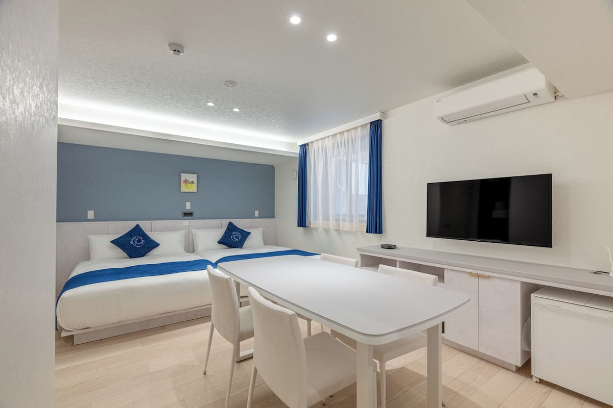 A modern hotel room with a bed, a desk, a TV, and a window with curtains.