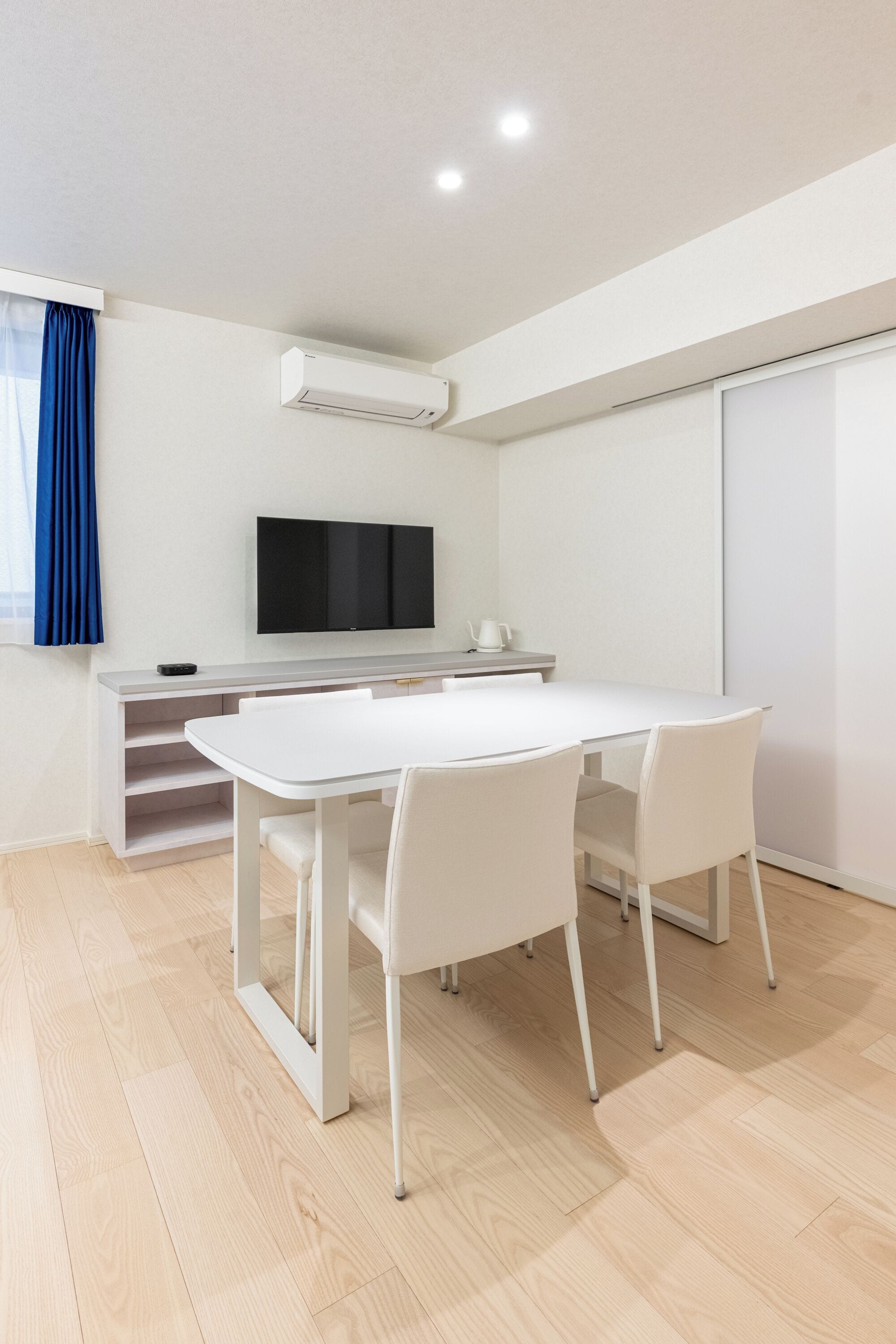 A modern room with a white table, chairs, a flat-screen TV, and a sliding door.