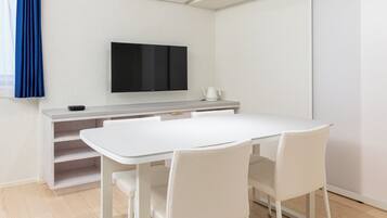 A modern room with a white table, chairs, a flat-screen TV, and a sliding door.