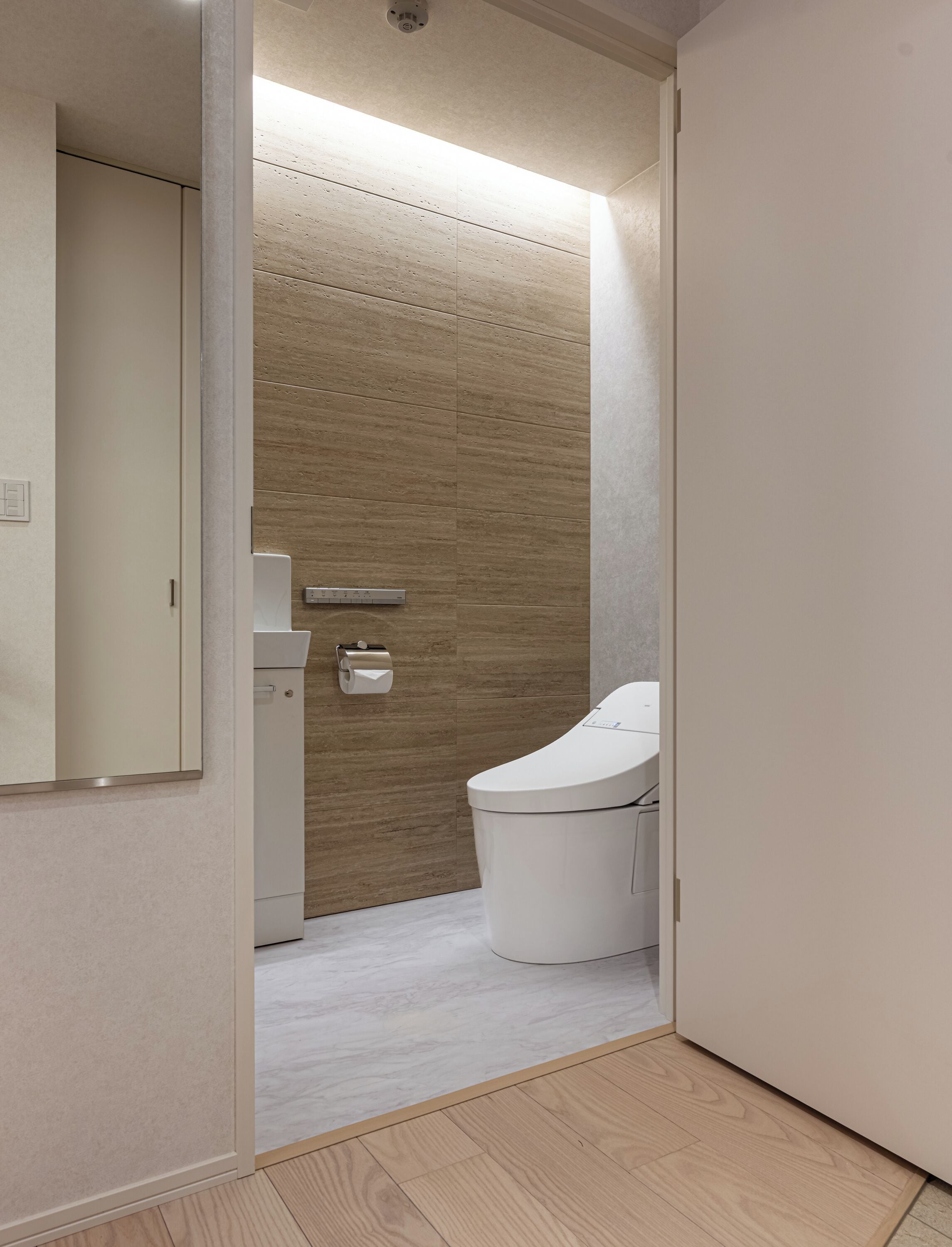 A narrow hallway with a toilet, a small cabinet, and a mirror.