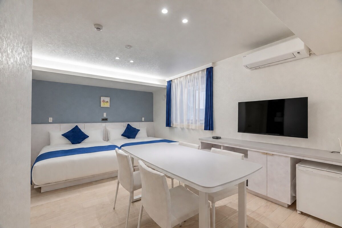 A hotel room with a bed, a desk, a chair, a television, and an air conditioning unit.
