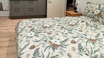 A bedroom with a floral bedspread, a grey dresser, and a door leading to another room.