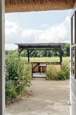A covered outdoor area with a wooden bench and a pergola, surrounded by greenery and a field. - Nostalgic charm in a yellow timber house (Sakskøbing)