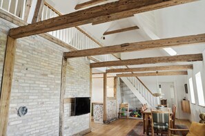 Un loft espacioso con vigas de madera a la vista, pared de ladrillo, escalera y comedor con sillas y mesa.
