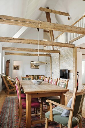 Un comedor con una mesa y sillas de madera, una lámpara colgante y una pared de ladrillo.