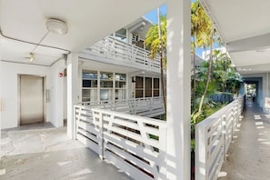 A modern hotel corridor with white railings, a double-height balcony, and a view of palm trees. - Sunny Studio with Great Location, Smart TVs & Fully Equipped Kitchen (Miami Beach)