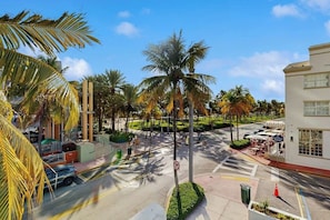 A street view with palm trees, a crosswalk, and a building with outdoor seating. - Sunny Studio with Great Location, Smart TVs & Fully Equipped Kitchen (Miami Beach)