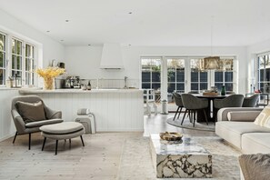 A modern kitchen with white cabinetry, a dining area with a round table and chairs, and a living room with a sofa and ottoman.