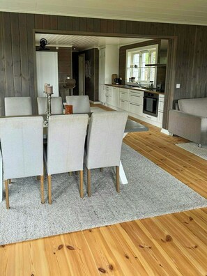 A modern living room with a dining area, wooden flooring, and a kitchen visible through an open doorway. - Modern cabin near family beaches in Holmsbu (Holmsbu)