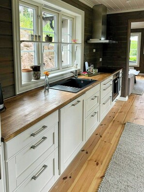 A kitchen with a large window, wooden countertops, and white cabinetry. - Modern cabin near family beaches in Holmsbu (Holmsbu)