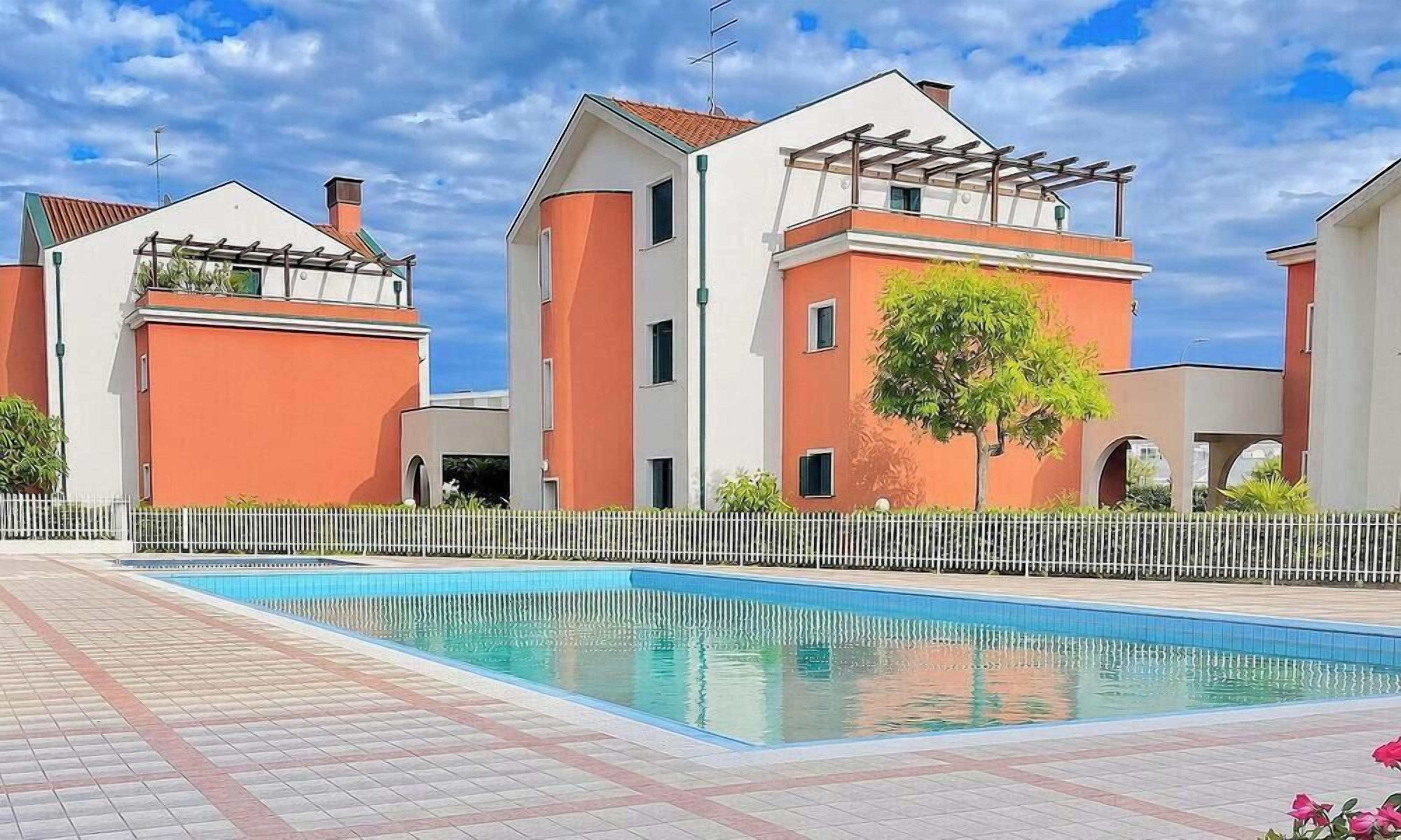 A residential building with a swimming pool, white fences, and a clear sky.