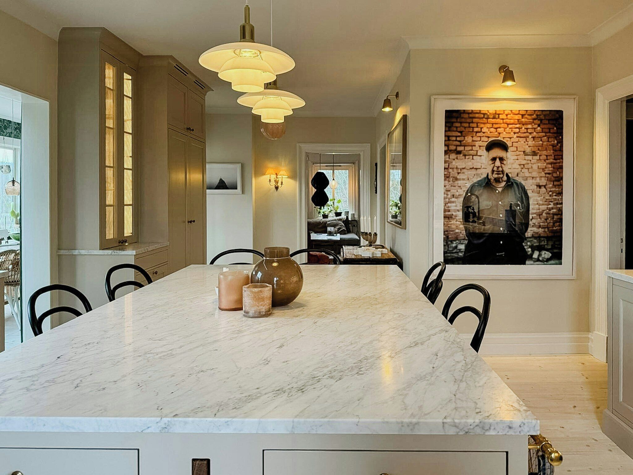 Una cocina moderna con una isla de mármol, iluminación colgante y un cuadro grande en la pared.