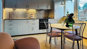 A modern kitchen with grey cabinets, a tiled backsplash, and a dining area with a round table and metal chairs. - Colorful character and charm by Nakskov Fjord (Nakskov)