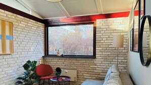 A cozy room with a brick wall, a window with a view, a red chair, a grey sofa, and a small table with a plant. - Colorful character and charm by Nakskov Fjord (Nakskov)