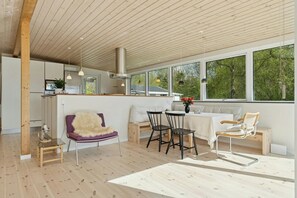 A modern kitchen with wooden cabinets, a dining area with a table and chairs, and large windows offering a view of trees. - Holiday home with views over Arresø lake (Frederiksværk)