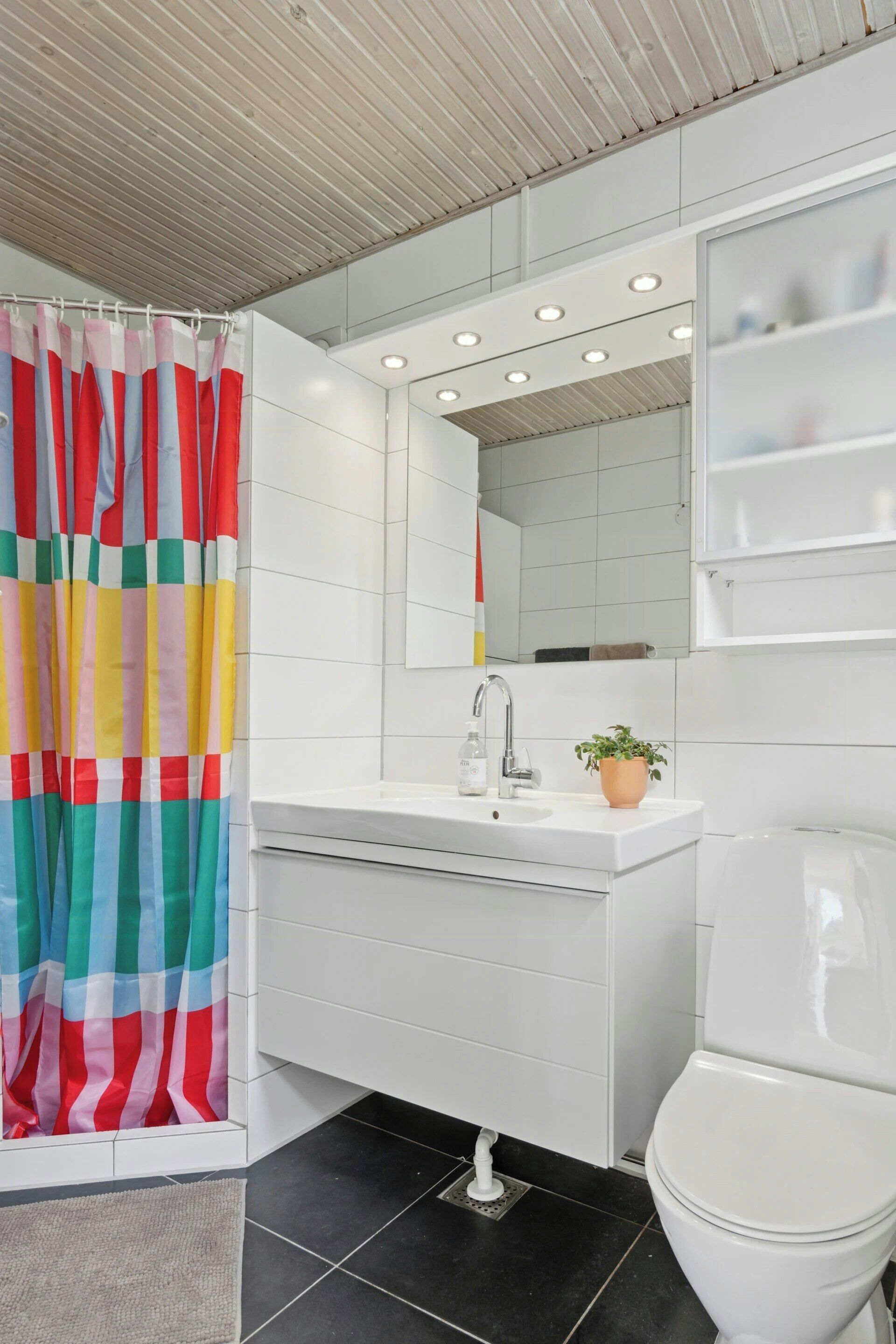 A modern bathroom with a shower curtain, a sink with a mirror, a toilet, and a potted plant.