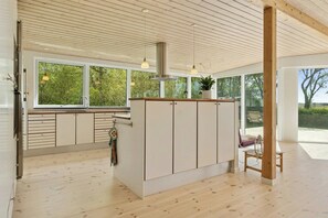 A modern kitchen with wooden cabinets, a central island, and large windows offering a view of greenery. - Holiday home with views over Arresø lake (Frederiksværk)