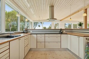 A modern kitchen with wooden cabinets, a large window, and a view of trees. - Holiday home with views over Arresø lake (Frederiksværk)