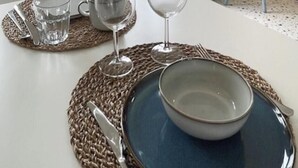 A dining table set with a bowl, wine glasses, and cutlery on woven placemats.