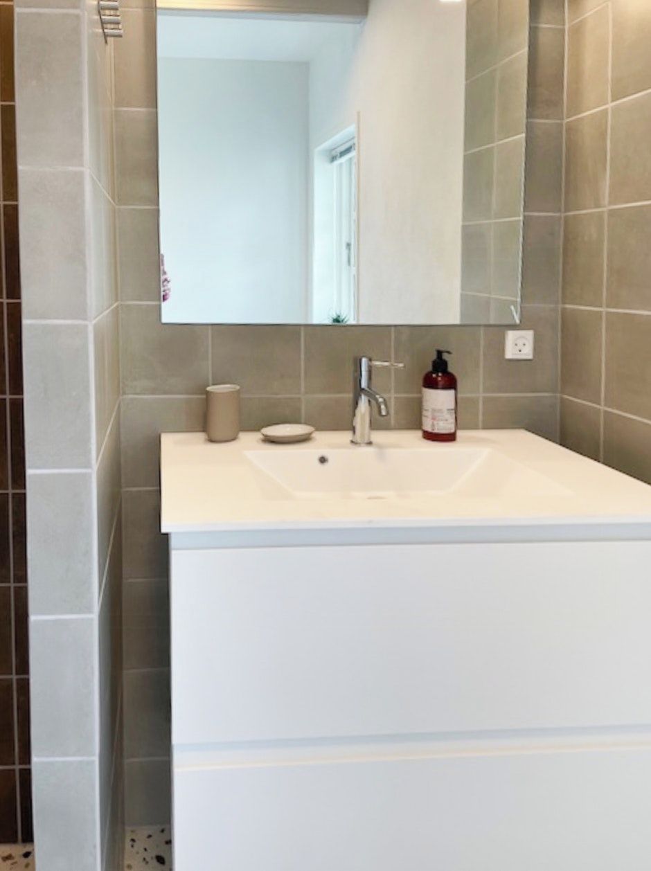 A bathroom with a white sink, a mirror, and a red bottle of soap.